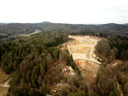 Blick über die Höhlenruine von Hunas und den angrenzenden Steinbruch. Der Fundplatz befindet sich neben dem umgestürzten Baum in der Bildmitte (Bild: C. Mischka).